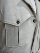Close-up of a light beige coat with pocket details and horn buttons.