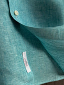 Close-up of a teal fabric with a pearl button and Albini 1876 label.