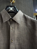 Close-up of grey shirt collar and mother-of-pearl buttons, showing bespoke craftsmanship and luxury details.